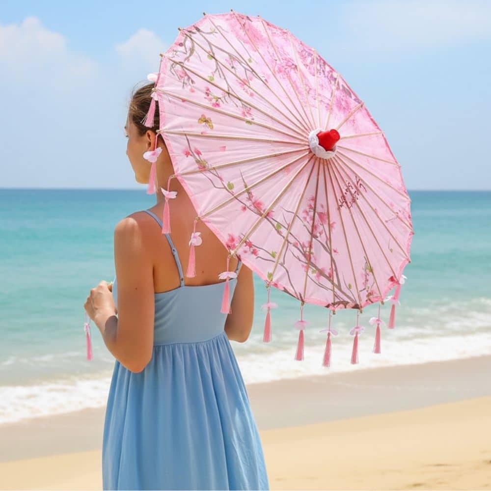 Femme portant une ombrelle anti-UV rose ornée de fleurs, face à la mer sous un ciel bleu