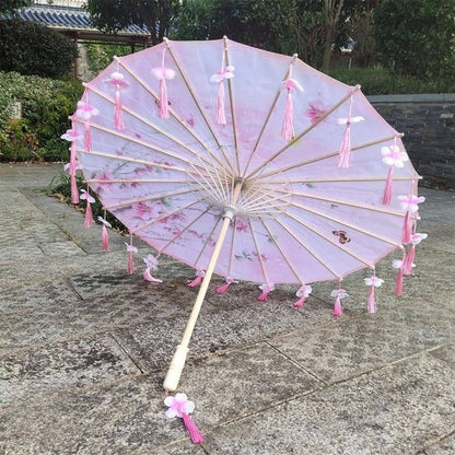 Ombrelle anti UV universelle rose avec motifs floraux, franges et décorations en tissu, posée sur un sol en pierre