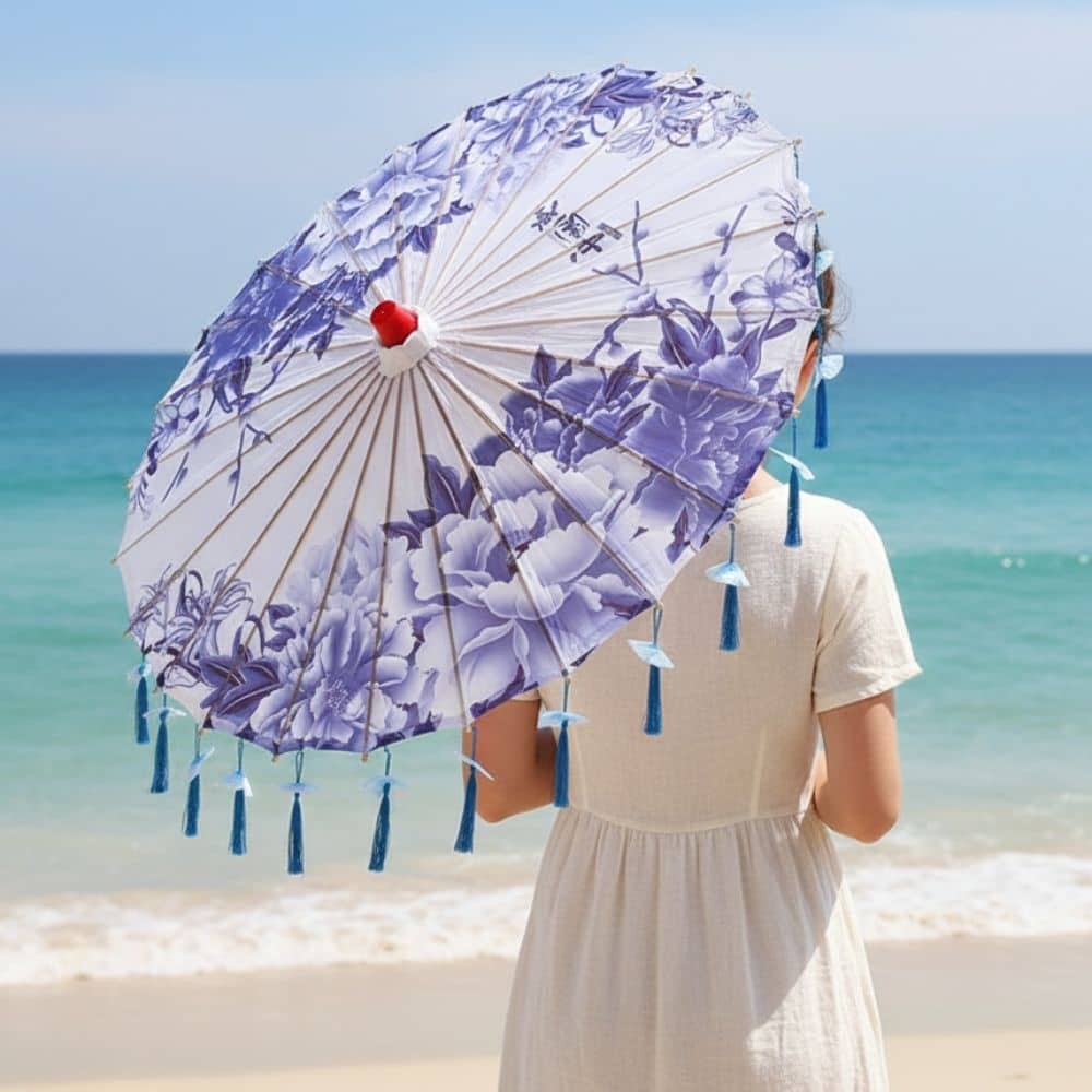 Ombrelle anti-UV violette ornée de motifs floraux, tenue par une personne sur une plage ensoleillée