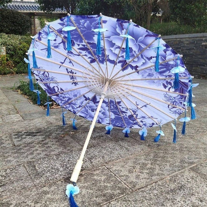 Ombrelle anti-UV violette ornée de motifs floraux, avec des franges bleues et un décor naturel en arrière-plan