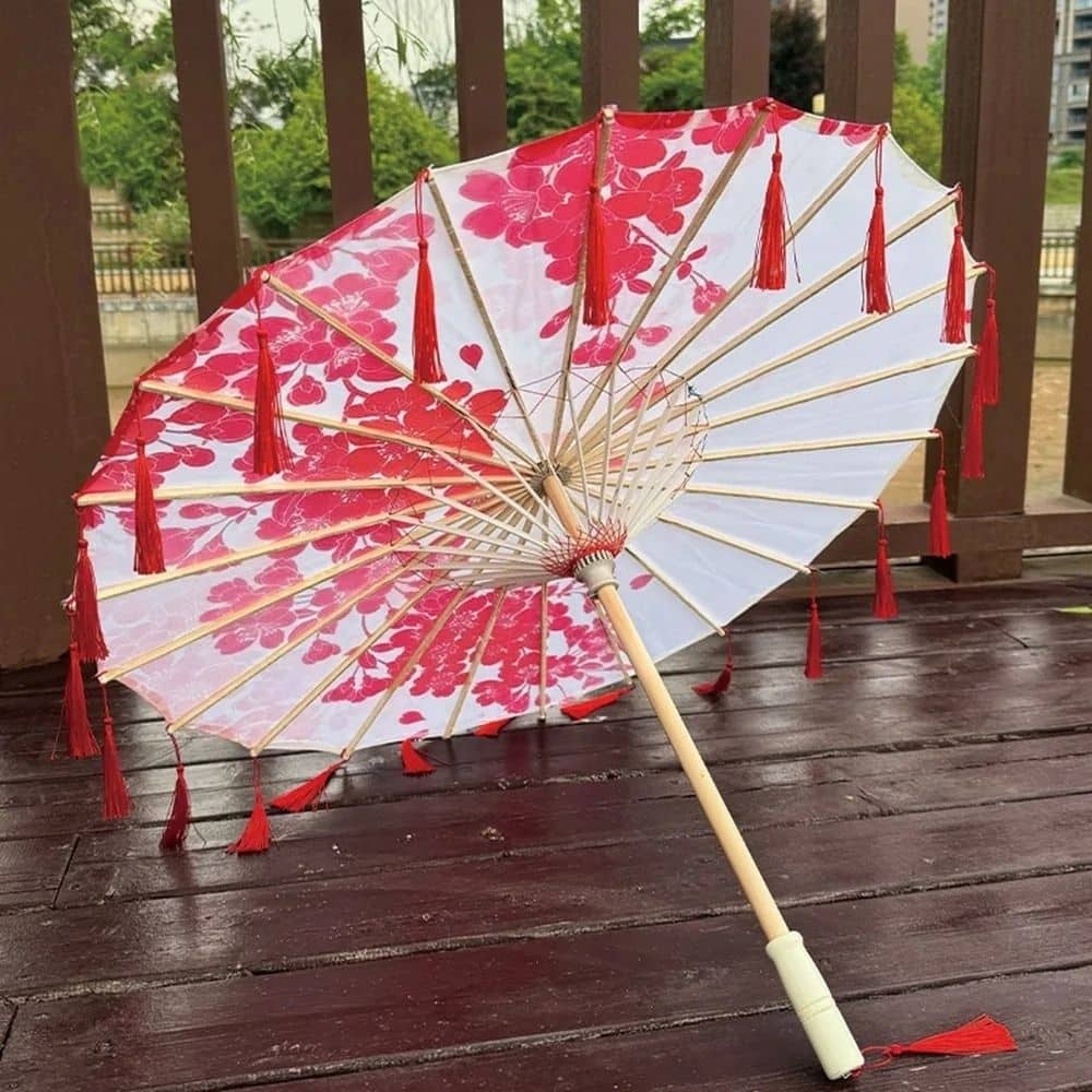 Ombrelle blanche décorée de fleurs rouges et de franges, posée sur un sol en bois