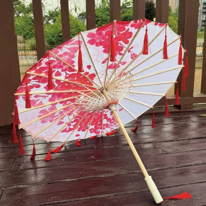 Ombrelle blanche décorée de fleurs rouges et de franges, posée sur un sol en bois