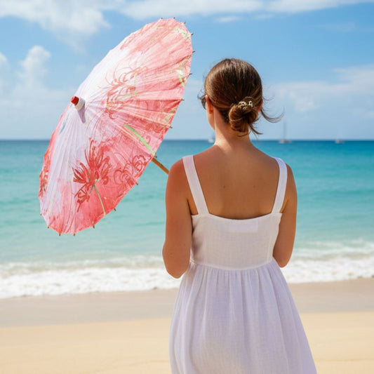 Femme vue de dos tenant une ombrelle rose, vêtue d'une robe blanche, sur une plage ensoleillée