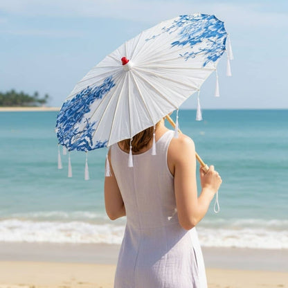 Ombrelle blanche ornée de motifs floraux bleus, tenue par une femme sur une plage ensoleillée