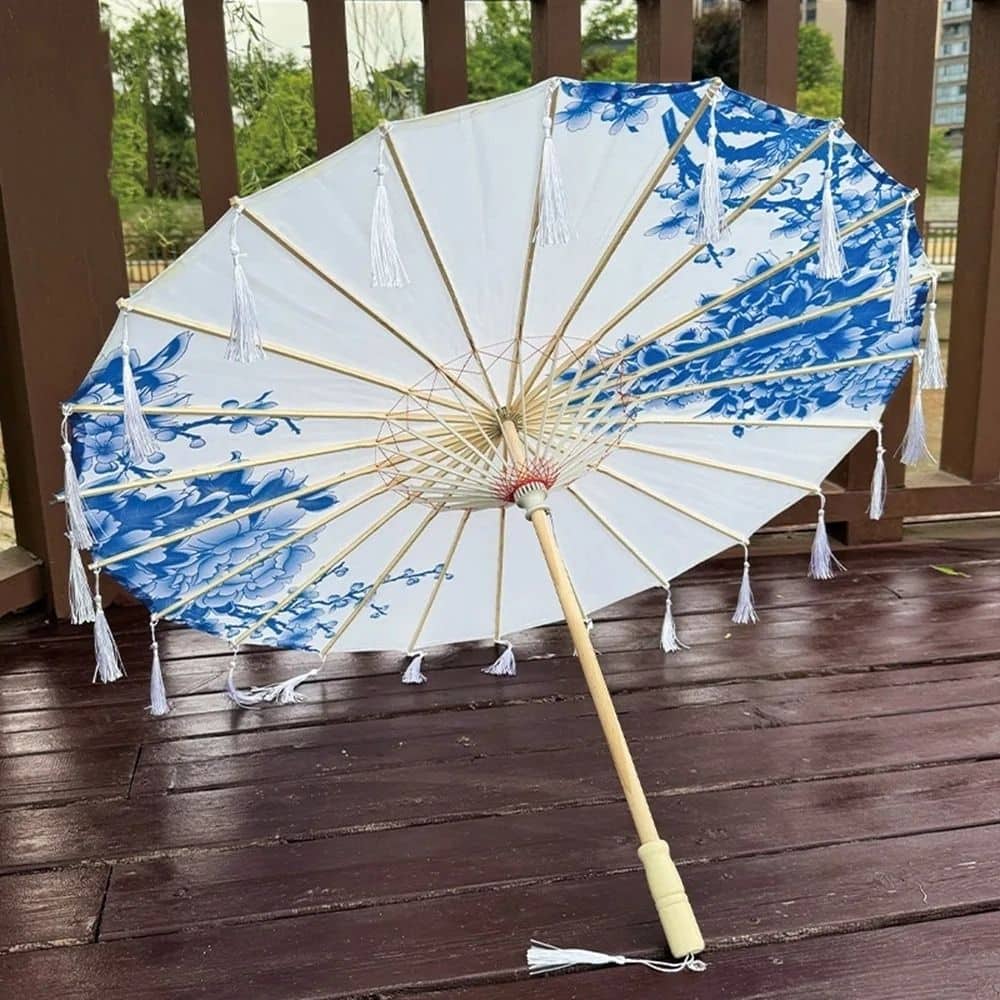 Ombrelle blanche ornée de motifs floraux bleus, avec une structure en bois et des franges blanches