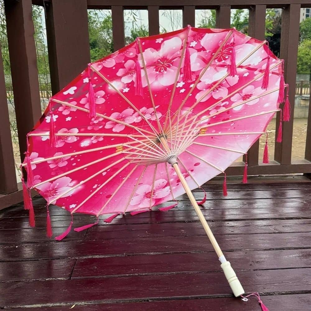 Ombrelle fleurie rose avec des motifs de fleurs, décorée de franges, posée sur un sol en bois