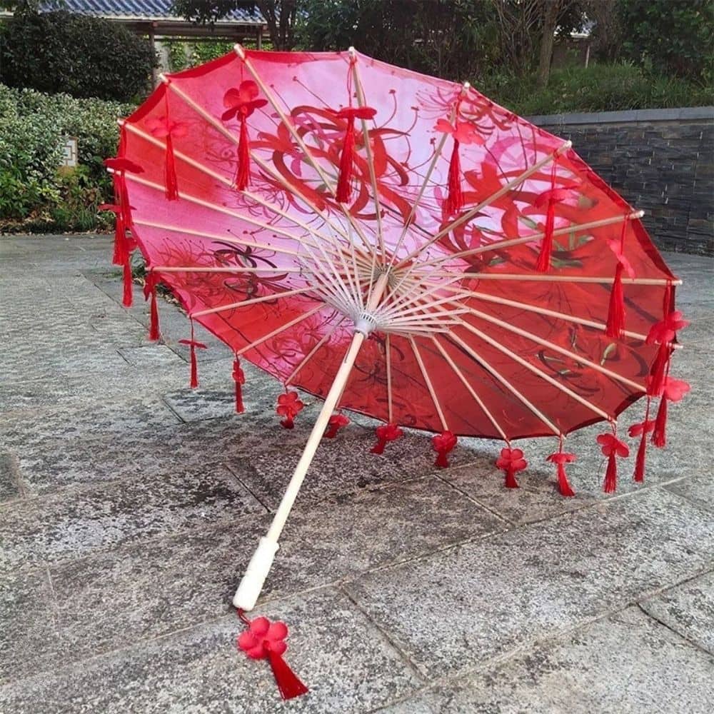 Ombrelle japonaise ancienne rouge ornée de motifs floraux, avec des pompons et des franges rouges, posée sur un sol en