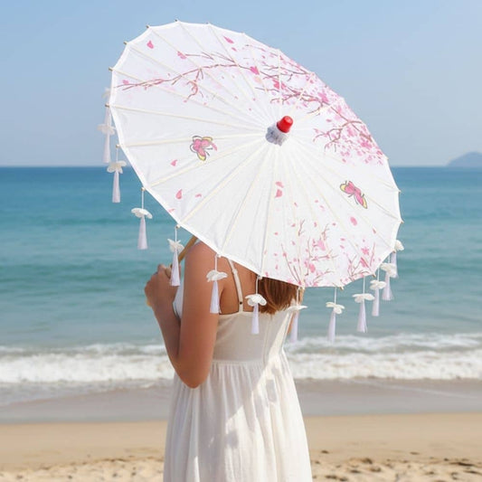 Ombrelle japonaise blanche ornée de motifs floraux, utilisée sur une plage ensoleillée avec des vagues en arrière-plan