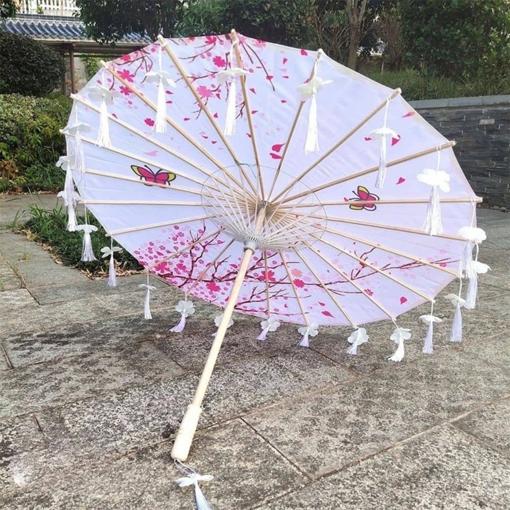 Ombrelle japonaise blanche ornée de motifs floraux roses et de papillons, posée sur un sol en pierre