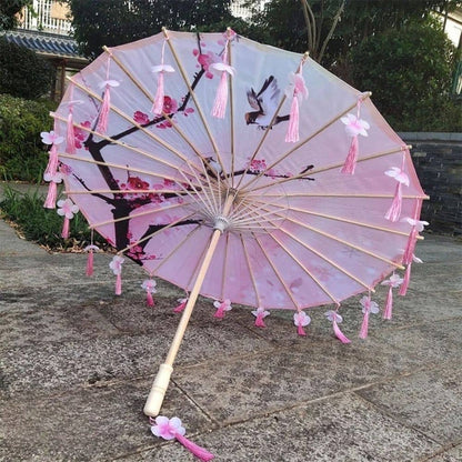 Ombrelle japonaise rose ornée de fleurs et de franges, posée sur un sol en pierre, entourée de verdure