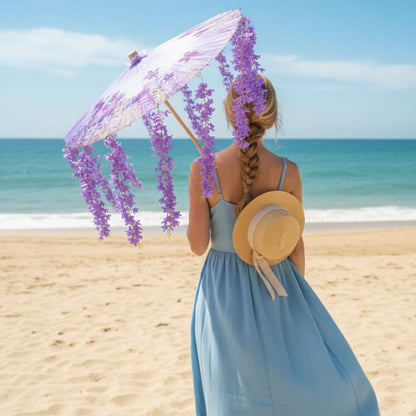 Femme de dos portant une robe bleue, tenant une ombrelle violette décorée de fleurs, sur une plage ensoleillée