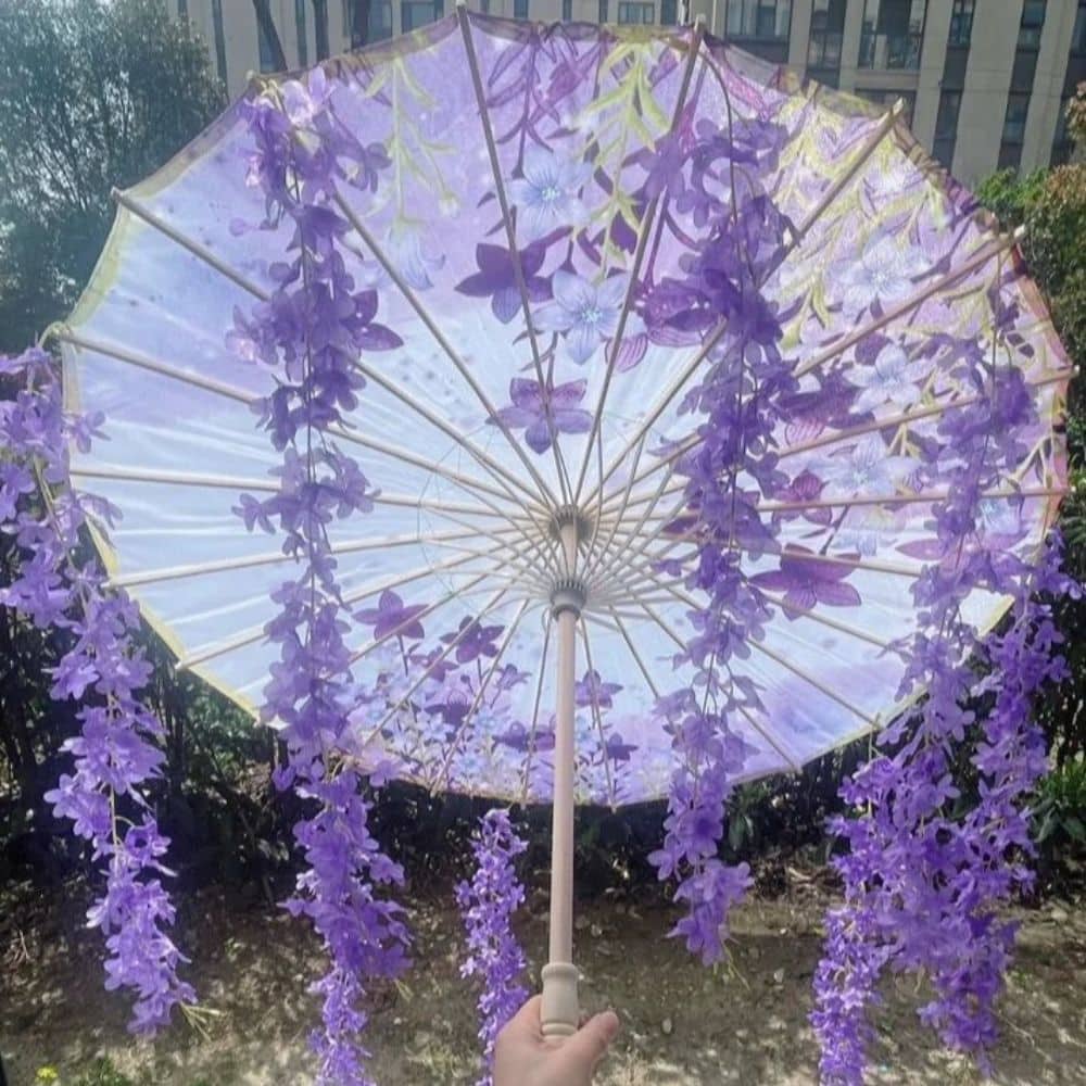 Ombrelle japonaise anti-UV violette ornée de fleurs et de motifs délicats, tenue à la main dans un décor verdoyant