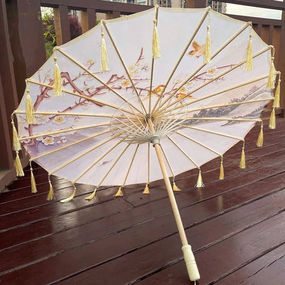 Ombrelle japonaise ornée de fleurs et de motifs délicats, avec des franges dorées, posée sur un sol en bois