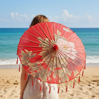 Une ombrelle rouge ornée de motifs floraux, tenue par une personne sur une plage ensoleillée
