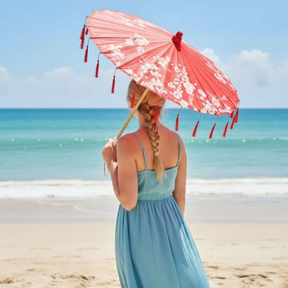 Femme de dos portant une ombrelle japonaise rouge, vêtue d'une robe bleue, face à la mer turquoise