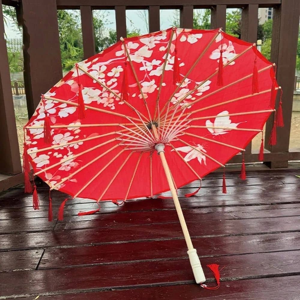 Ombrelle japonaise rouge ornée de fleurs blanches, posée sur un sol en bois verni, avec des franges décoratives