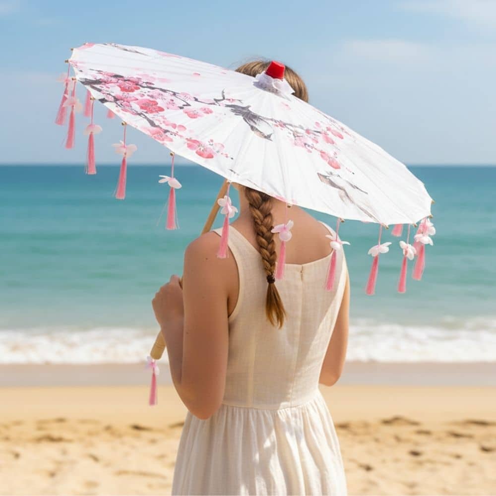 Ombrelle parapluie anti UV rose ornée de fleurs, tenue par une jeune femme sur une plage ensoleillée