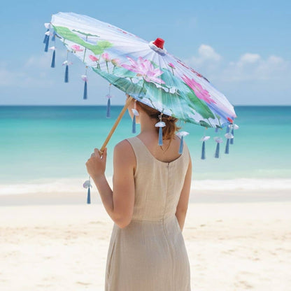 Femme debout sur la plage tenant une ombrelle pliante aux motifs floraux, sous un ciel bleu clair
