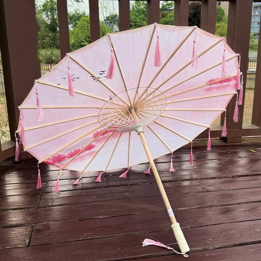 Ombrelle pour femme de couleur rose avec des franges, motif floral et structure en bois sur un fond en bois