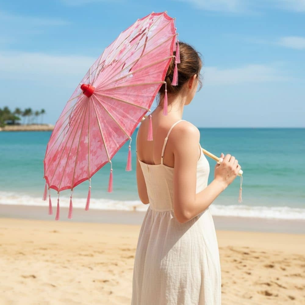 Femme portant une ombrelle rose à franges, debout sur la plage avec la mer en arrière-plan