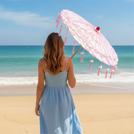 Femme vue de dos sur la plage, tenant une ombrelle rose à motifs floraux sous un ciel bleu