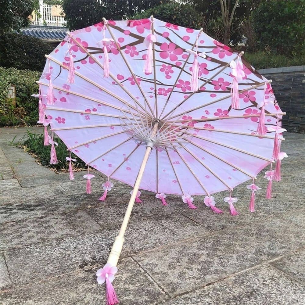 Ombrelle de style japonais rose ornée de fleurs et de pompons, posée sur un sol en pierre