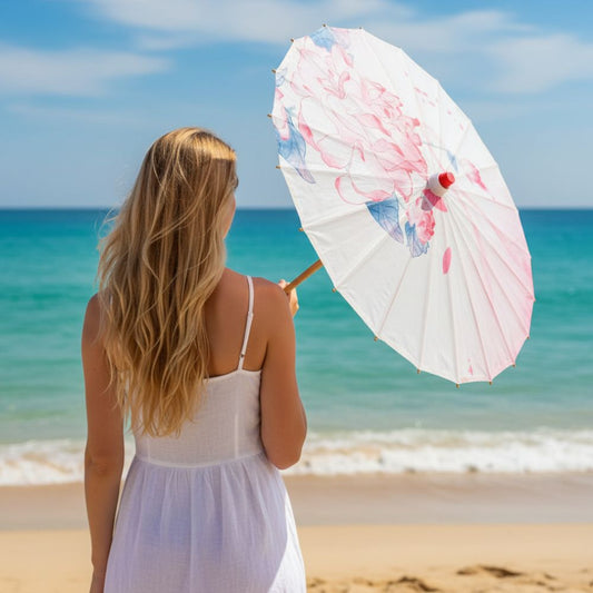 Femme aux cheveux longs tenant une ombrelle japonaise blanche avec des motifs floraux, face à la mer turquoise