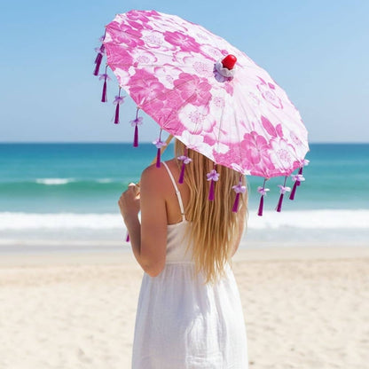 Ombrelle anti-UV rose ornée de fleurs, avec des franges violettes, tenue par une femme sur une plage ensoleillée