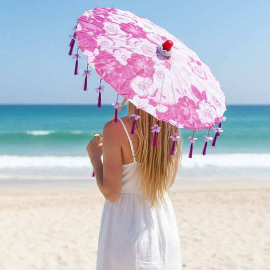 Ombrelle anti-UV rose ornée de fleurs, avec des franges violettes, tenue par une femme sur une plage ensoleillée