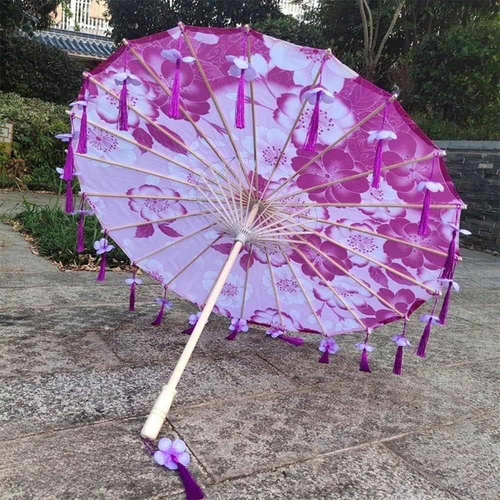 Ombrelle anti-UV rose avec des motifs floraux, ornée de franges violettes et d'une tige en bois