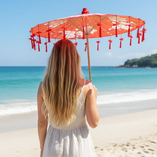 Femme avec une ombrelle rouge à franges, se tenant sur une plage face à la mer turquoise