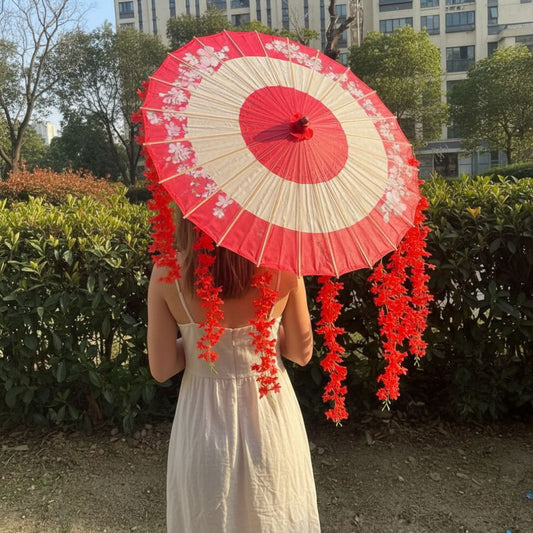 Une ombrelle rouge et blanche ornée de fleurs, tenue par une femme en robe légère, se détache sur un décor