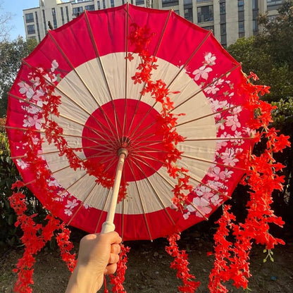 Ombrelle rouge et blanche ornée de fleurs, tenue à la main, avec un décor urbain en arrière-plan