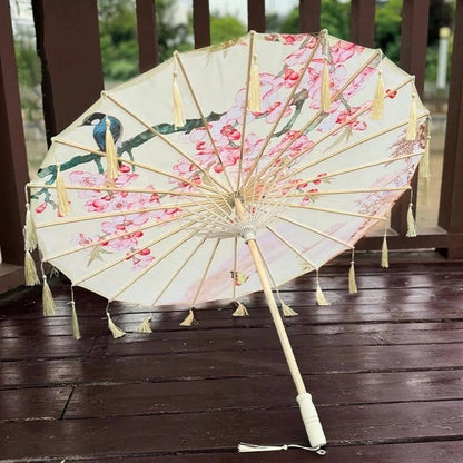 Ombrelle anti-UV beige et rose ornée de fleurs, avec des franges et un manche en bois clair sur un sol
