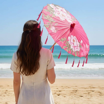 Une femme de dos tient une ombrelle japonaise rose ornée de fleurs, face à la mer et au ciel bleu