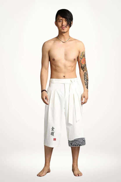 Homme debout portant un pantalon kimono blanc avec un motif noir, décor minimaliste et ambiance zen