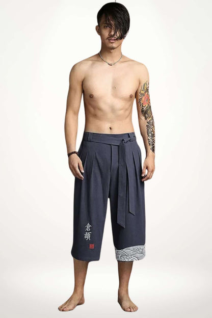 Homme portant un pantalon kimono bleu foncé, décoré de motifs blancs, dans une posture décontractée sur fond neutre