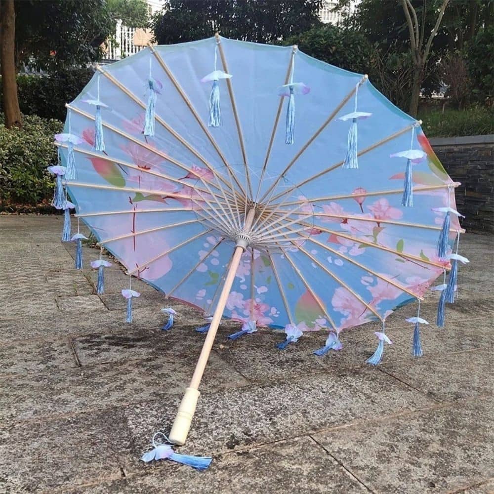 Parapluie japonais bleu avec des motifs floraux et des franges en satin, posé sur un sol en pierre