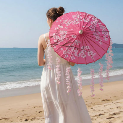 Femme de dos portant un kimono blanc, tenant un parapluie japonais rose décoré de fleurs, sur une plage ensoleillée