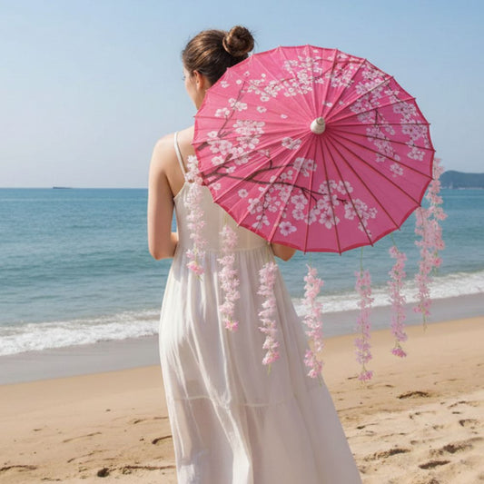 Femme de dos portant un kimono blanc, tenant un parapluie japonais rose décoré de fleurs, sur une plage ensoleillée