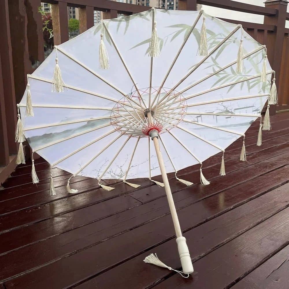 Parapluie japonais traditionnel blanc avec des franges, posé sur un sol en bois, décoré de motifs de bambou