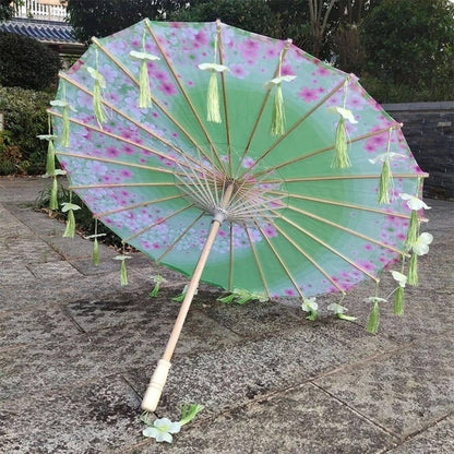 Parapluie ombrelle anti-UV vert décoré de fleurs roses et de franges vertes, posé sur un sol en pierre