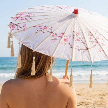 Un parapluie traditionnel japonais blanc orné de fleurs roses, tenu par une personne sur la plage ensoleillée