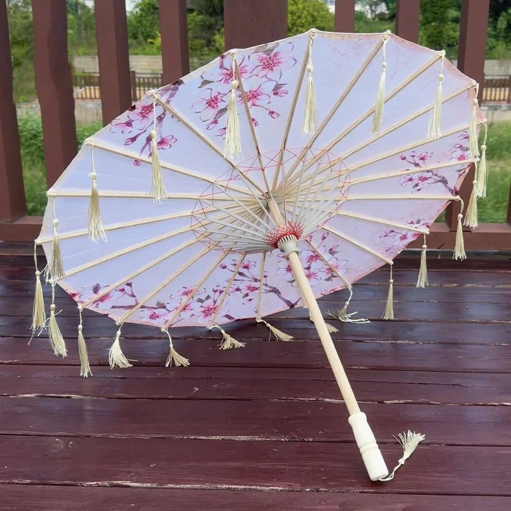 Parapluie traditionnel japonais blanc avec motifs de fleurs roses et franges, reposant sur un sol en bois