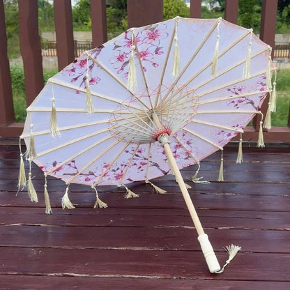Parapluie traditionnel japonais blanc avec motifs de fleurs roses et franges, reposant sur un sol en bois