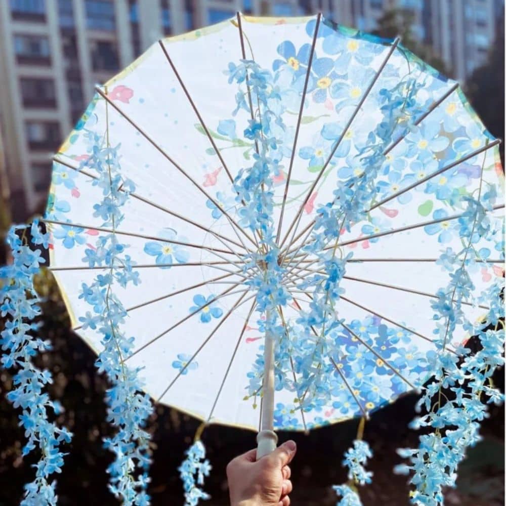 Parapluie traditionnel japonais bleu ciel décoré de fleurs, tenu à la main avec des détails délicats en tissu