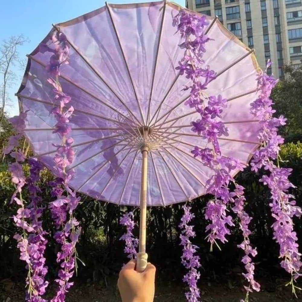 Parapluie UV violet décoré de fleurs violettes, tenu à la main, avec un fond de verdure