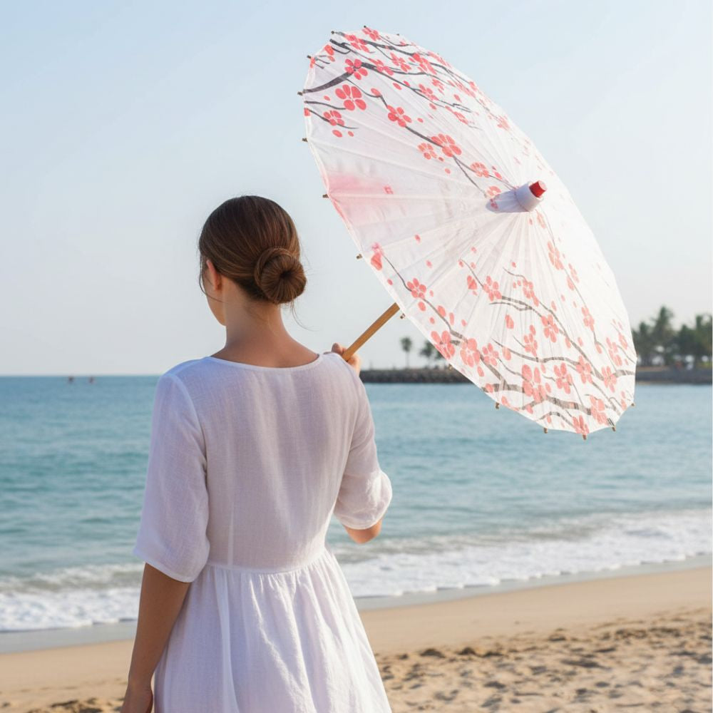 Femme portant un parasol ombrelle japonais blanc avec des motifs floraux rouges, face à la mer