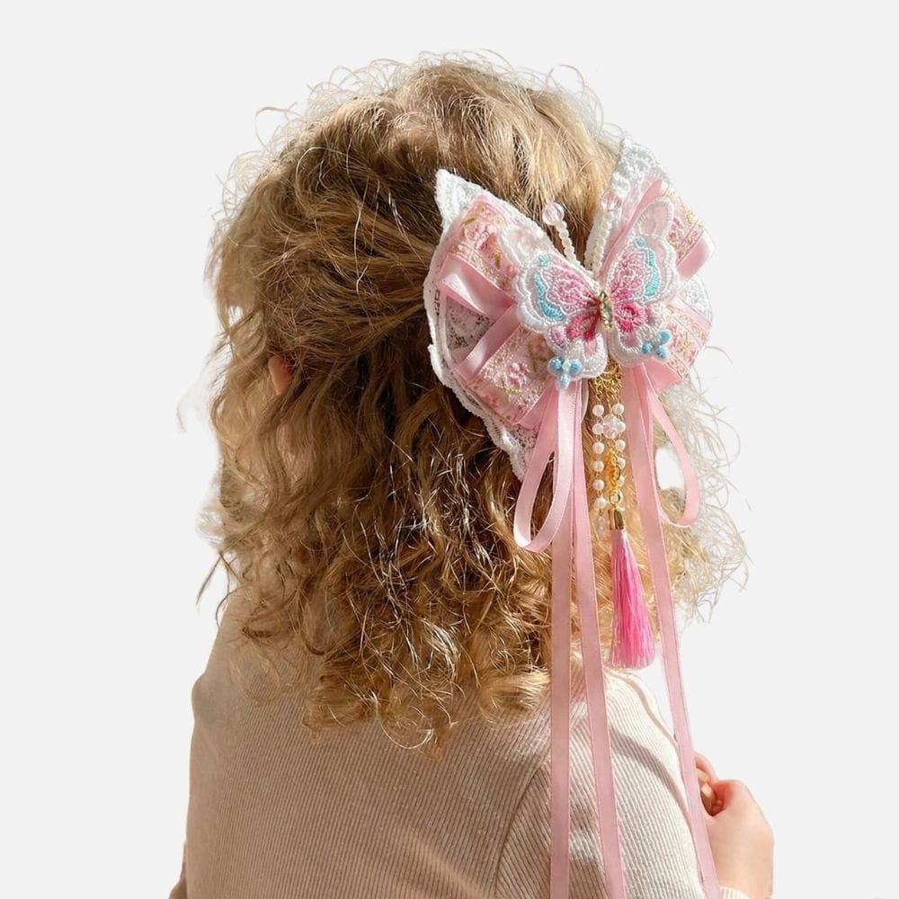 Un nœud en satin rose orné d'un papillon coloré et de perles, sur des cheveux bouclés