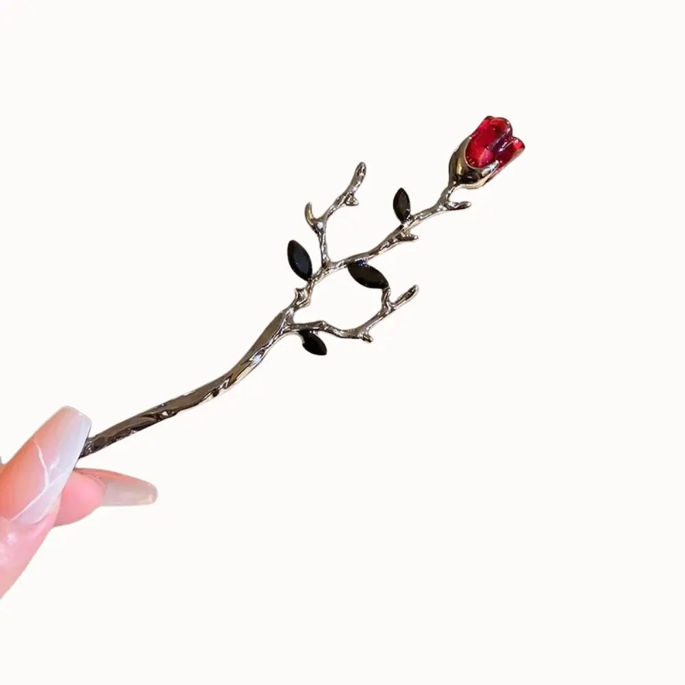 Épingle à tige sombre surmontée d’une rose rouge.